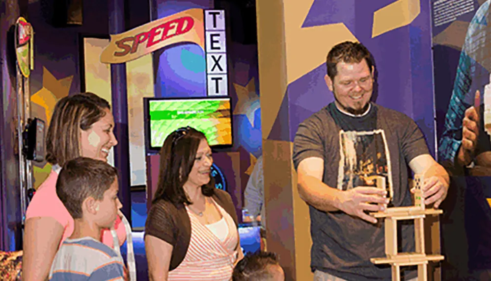 A group of people including a man building a tower from wooden blocks are engaged in an interactive activity at what appears to be a colorful and vibrant exhibit or event