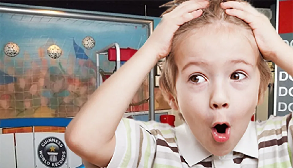 A surprised young child is wide-eyed and holding their head with their mouth open in front of a backdrop featuring the Guinness World Records logo