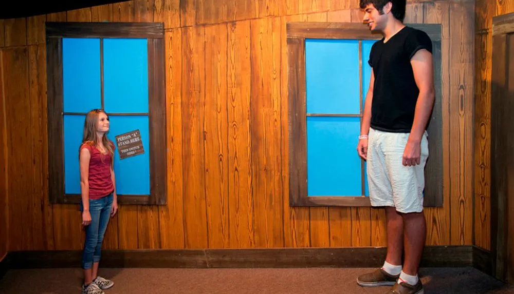 A man and a woman appear to be drastically different in size due to an optical illusion in a room designed with forced perspective