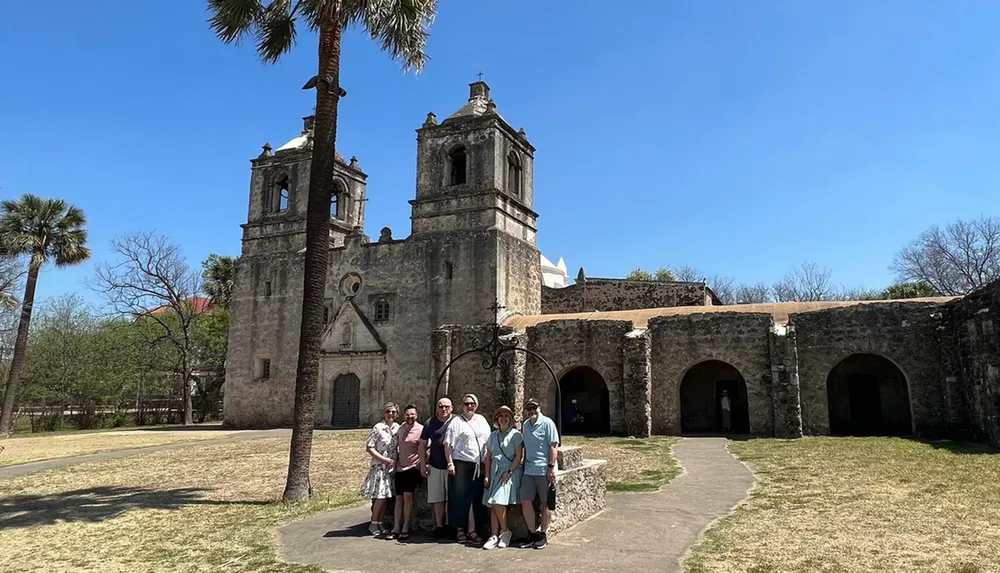 A group of people is posing for a photo in front of an old Spanish colonial church with a clear blue sky above them