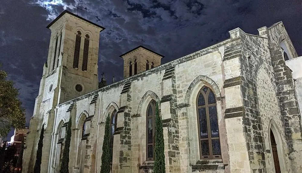 An ancient stone church stands illuminated at night under a dramatic cloudy sky