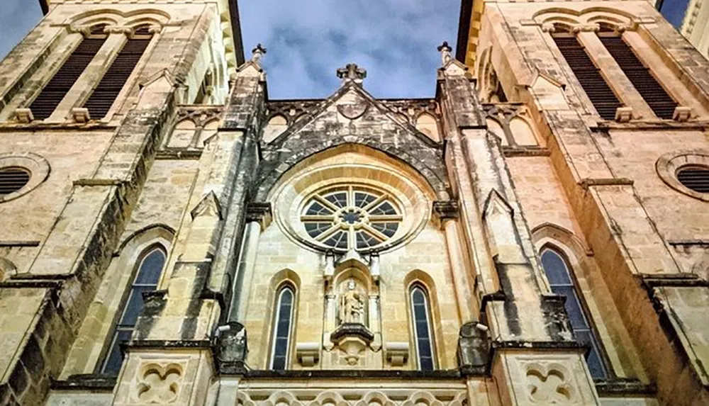The image shows the ornate facade of a gothic-style church with a large rose window and architectural details against a cloudy sky