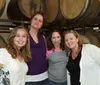 Four women are smiling for a photo in front of wooden barrels possibly at a winery or brewery
