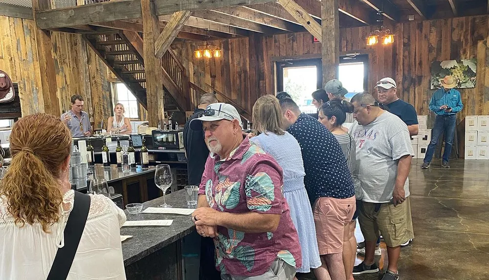 A group of people is gathered inside a rustic-styled building possibly a winery or tasting room with some waiting at the counter and others engaged in conversation