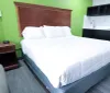 The image shows a neatly made bed in a hotel room with green walls wood and black furnishings and a gray floor
