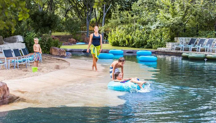 A family enjoys a sunny day at a lazy river with children playing in the water and an adult supervising