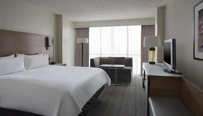 This image shows a neatly arranged modern hotel room with a large bed a sitting area and a flat-screen TV on a desk