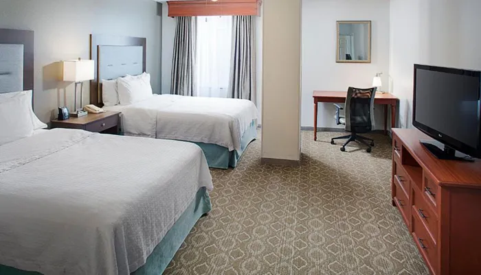 The image shows a well-kept hotel room with two beds a desk with a chair and a television set creating a comfortable and functional space for guests