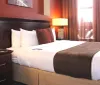 This is an image of a neatly arranged hotel room with a large bed nightstands with lamps and a warm color scheme
