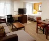 The image shows a modern hotel room with two beds a work desk with a chair a television and warm inviting decor