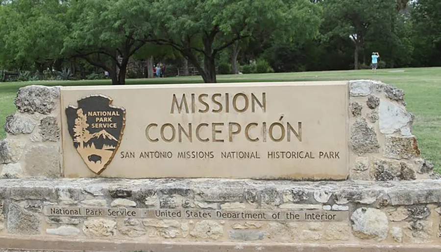 The image shows a sign for Mission Concepción, part of the San Antonio Missions National Historical Park, managed by the National Park Service and the United States Department of the Interior.