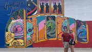 A couple is posing in front of a vibrant and colorful mural with the text 