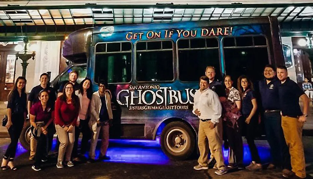 A group of people are posing for a photo in front of a bus that is advertised for a ghost tour in San Antonio