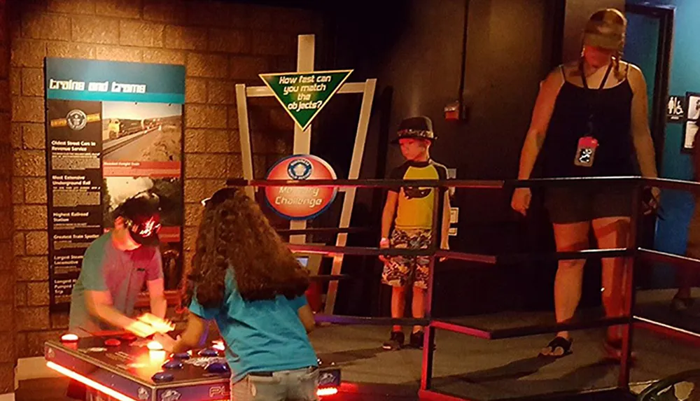 Two people are engaging in a reaction time game at an interactive exhibit while a child and an onlooker watch