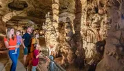 A family is observing the intricate formations inside a beautifully lit cavern.