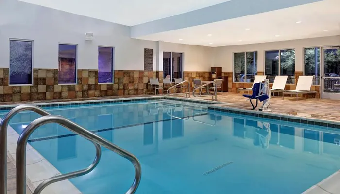 The image shows an indoor swimming pool with a surrounding seating area and a wheelchair-accessible pool lift