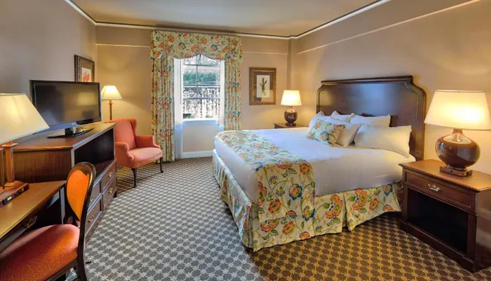 The image shows a well-appointed hotel room with a floral bedspread traditional furniture and a view outside the window