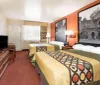 The image shows a tidy hotel room with two double beds patterned bed covers an orange accent wall with large black and white photographs and an adjoining bathroom visible in the background