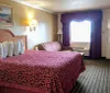 The image shows a standard hotel room with two double beds featuring red patterned bedspreads simple decor and basic furnishings