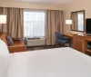 This is a neatly arranged hotel room featuring a king-sized bed a desk with a chair a television and lamps for lighting