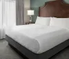 The image shows a neatly made bed with white linens in a tidy room with a classic decor style featuring a large headboard bedside tables and lamps