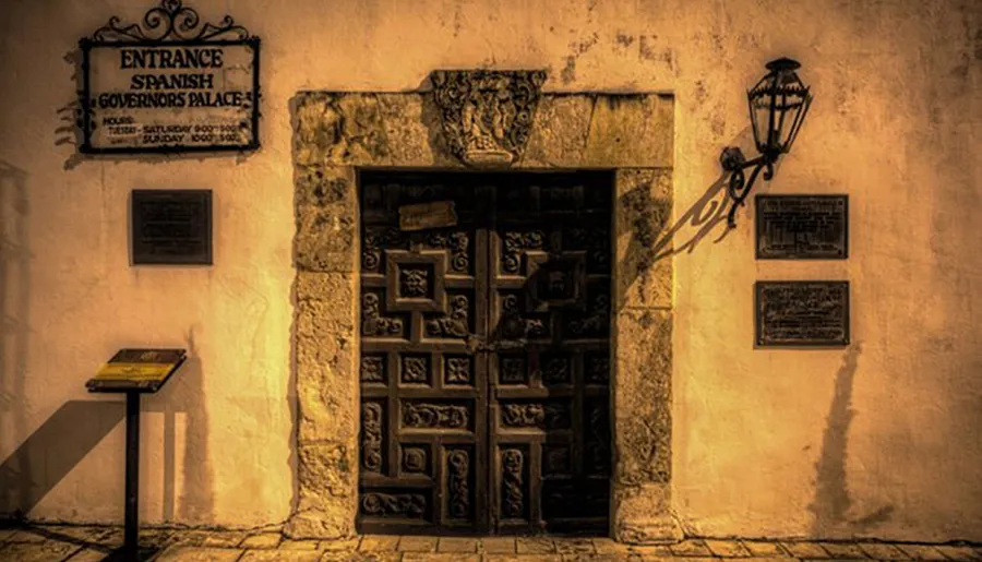 The image shows an ornate entrance door flanked by historical plaques and a lantern, labeled as the Spanish Governor's Palace, evoking an old-world ambiance.