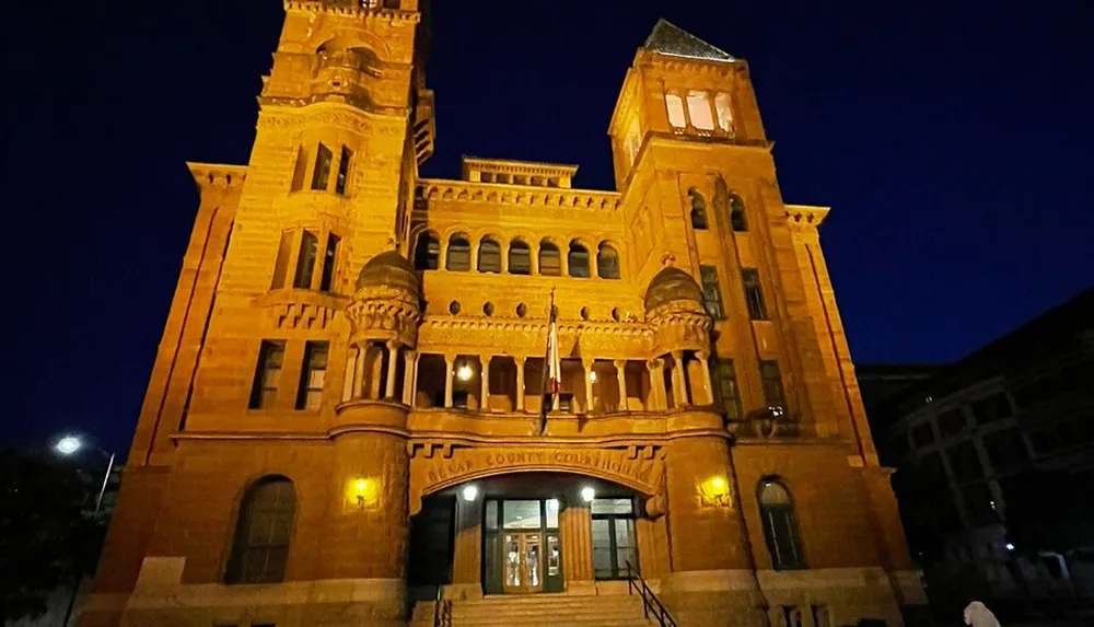 The image shows the illuminated facade of a grand sandstone courthouse at night with ornate architectural details and a clear sky