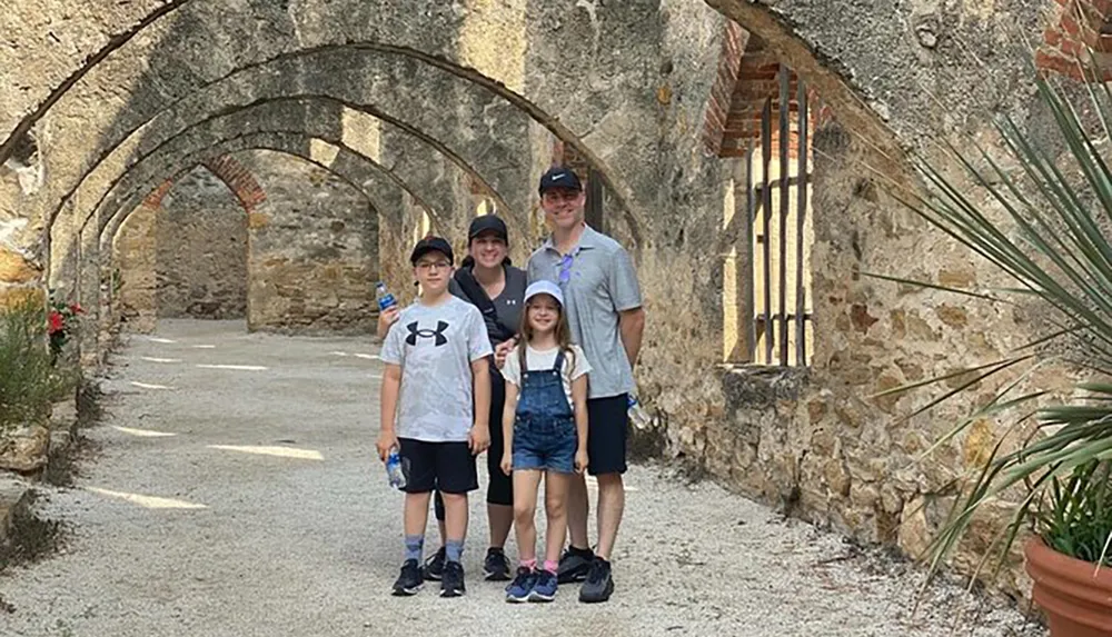 A family of four is smiling for a photo under a series of stone arches in a historical setting