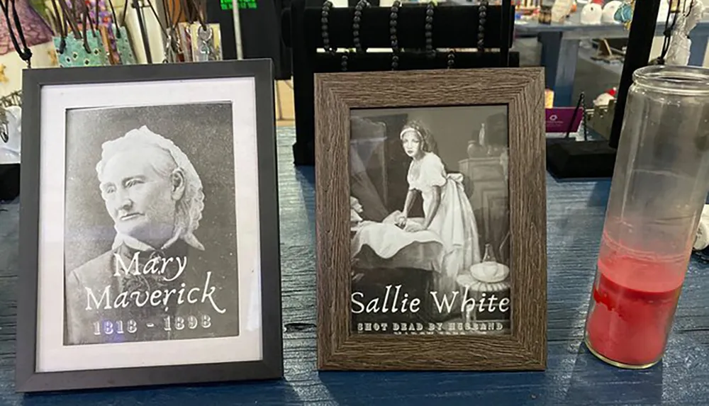 The image shows two framed black-and-white portraits one labeled Mary Maverick and another labeled Sallie White placed on a table next to a tall partially filled red drink