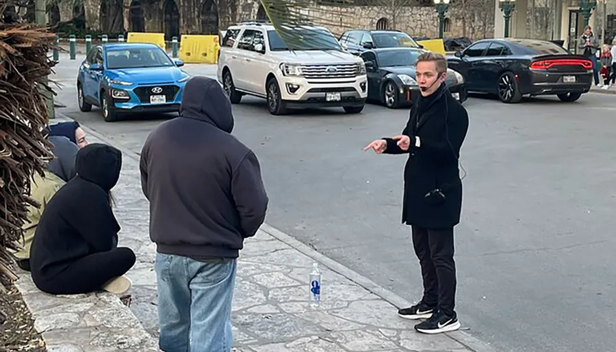 A person appears to be performing an outdoor demonstration or speaking to a small group on the street, with a plastic bottle standing upright on the pavement.