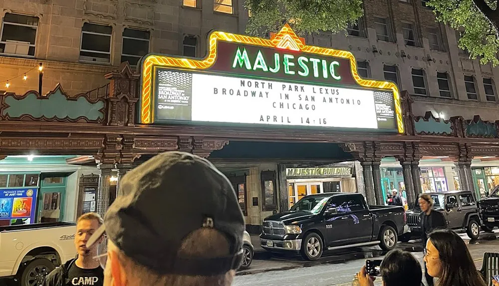 People are gathered outside the Majestic theater at night which is advertising a Broadway show named Chicago scheduled for April 14-16