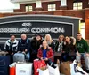 A group of smiling people with shopping bags are posing in front of the Woodbury Common Premium Outlets sign