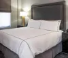 The image shows a neatly made bed with white linens in a modern hotel room with two bedside lamps and a phone