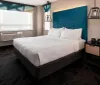 A modern hotel room featuring a large bed with a blue headboard clean white bedding unique hanging lamps and a window with a blurred city view