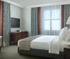 The image shows a neatly arranged hotel room with a large bed desk chair and wall decorations reflecting a comfortable and tidy guest accommodation