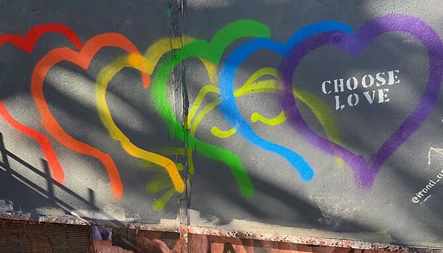 This image shows a colorful street art piece with a sequence of overlapping hearts in rainbow colors with the phrase CHOOSE LOVE painted in the center of the last heart.
