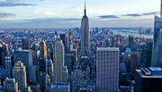 The image showcases a sweeping aerial view of New York City's skyline with the Empire State Building prominently centered and the Hudson River in the background.
