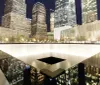 The image shows a serene night view of the 911 Memorial featuring one of the twin reflecting pools with illuminated skyscrapers rising in the background