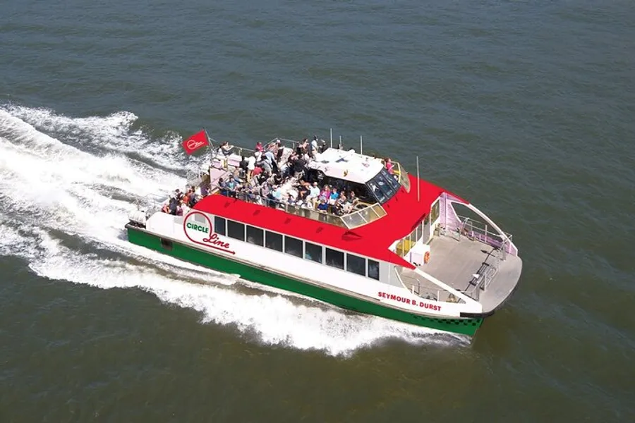 A group of passengers is enjoying a sunny day on an open deck of a red and green Circle Line sightseeing boat cruising on the water.