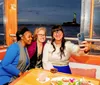 Three people are taking a selfie on a boat with the Statue of Liberty in the background at dusk