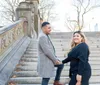 A couple shares an affectionate moment under an ornate arched passageway with a staircase in the background