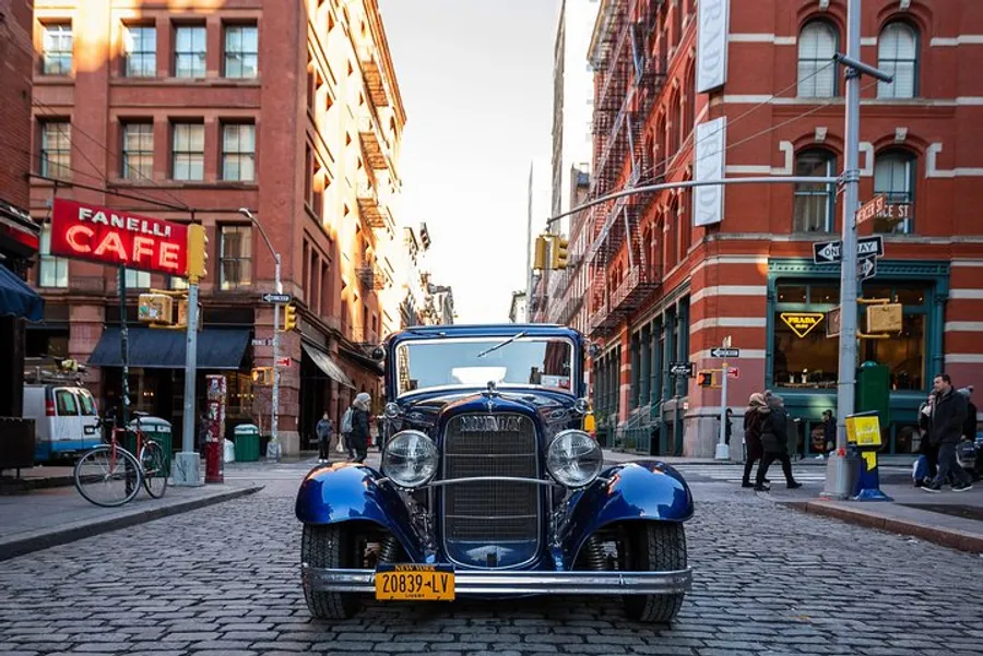 A vintage car is parked on a cobblestone street in an urban area with pedestrians and classic architecture, creating a scene that blends historical and modern elements.
