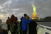 People on a boat are taking photos of the Statue of Liberty at twilight.