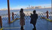 Two people are conversing on a ferry with the New York City skyline in the background.
