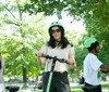 Two people wearing helmets are enjoying a ride on electric scooters near a historical archway in a park setting