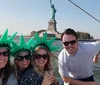 A group of people wearing Statue of Liberty crowns are smiling for a photo with the actual Statue of Liberty in the background likely enjoying a boat tour