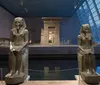 Two ancient Egyptian statues flank a water-filled channel leading to the Temple of Dendur set against a sloping glass wall and a modern museum interior