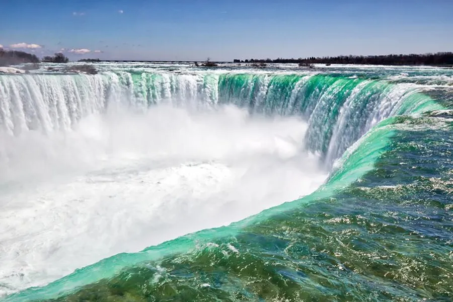 The image shows a majestic view of cascading water over the crest of Niagara Falls against a blue sky with scattered clouds.