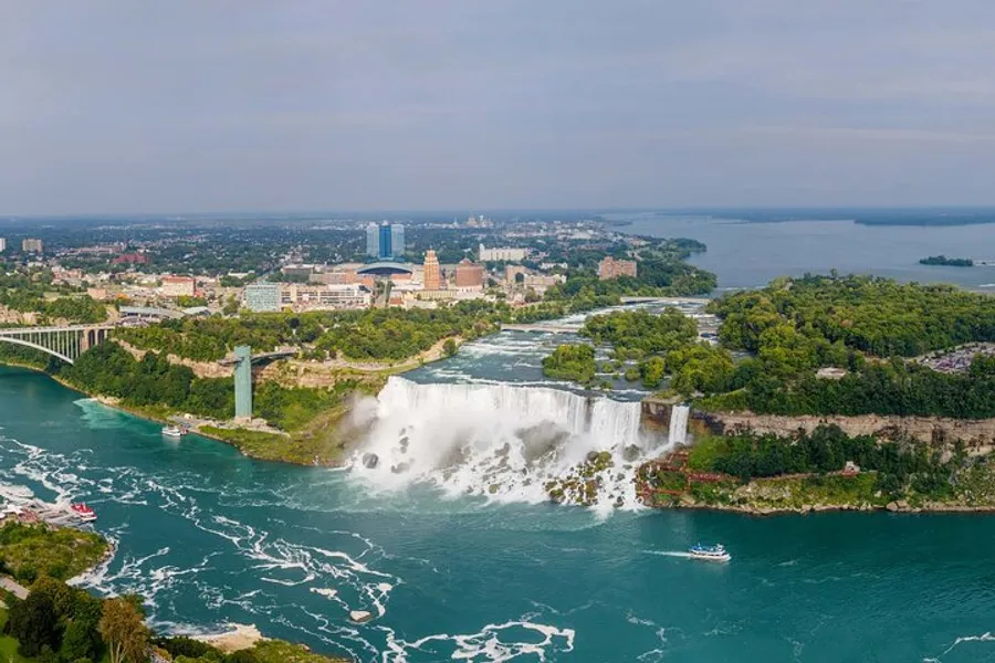 The image captures an aerial view of Niagara Falls with its cascading waters, a surrounding lush landscape, and nearby urban development.