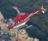 A red and white helicopter is flying over Central Park amidst the urban backdrop of a densely built cityscape